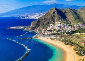 A beach in Tenerife with a yellow sandy beach, blue sea and mountains